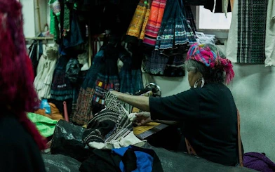 Local artisan sewing traditional garments in Sapa workshop during food tour experience.