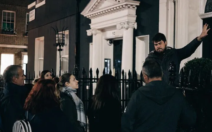 Group on York haunted walking tour listening to guide outside historic building at night.