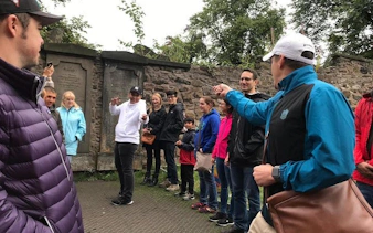 Group on Harry Potter walking tour in Edinburgh cemetery, guide leading themed trivia game.