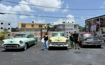 Classic cars parked in Little Havana, Miami, with visitors enjoying a guided walking tour.