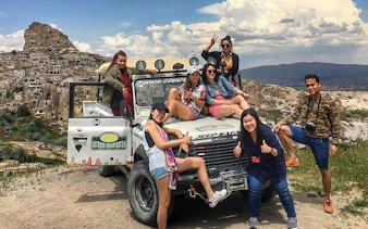 Cappadocia Jeep Safari group posing with jeep near rock formations.