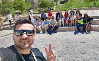 Group of tourists on Cappadocia Red Tour with guide, seated outdoors on stone steps.