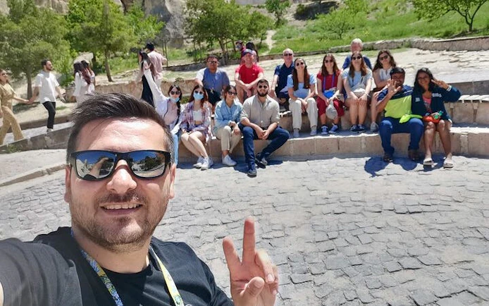 Group of tourists on Cappadocia Red Tour with guide, seated outdoors on stone steps.