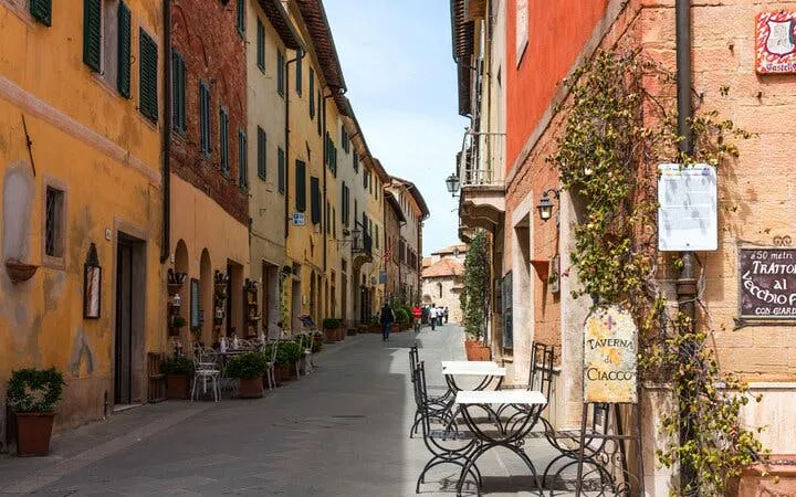 Narrow street in Siena with colorful buildings and outdoor café tables, part of self-guided city exploration game.
