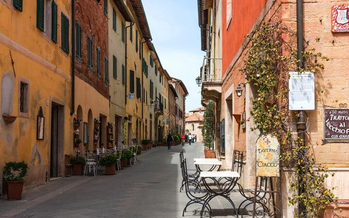 Narrow street in Siena with colorful buildings and outdoor café tables, part of self-guided city exploration game.