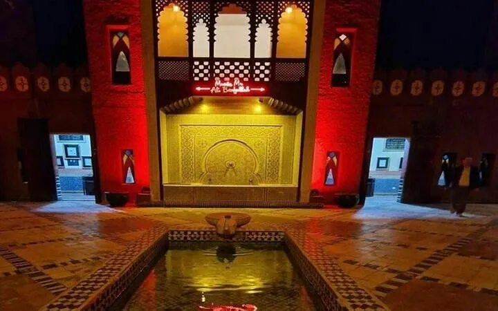 Chez Ali entrance with illuminated Moroccan architecture and fountain, Marrakesh.