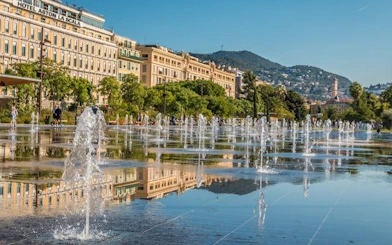Fountains in Promenade du Paillon, Nice, with cityscape and hills in the background.