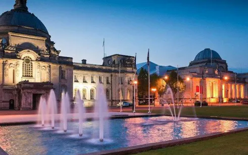 Cardiff City Hall and National Museum at dusk with illuminated fountains in the foreground.