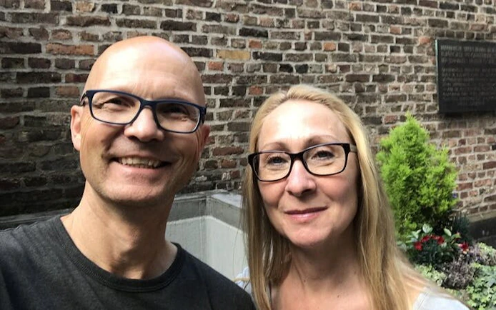 Two people smiling in front of a historic brick wall in Cologne.