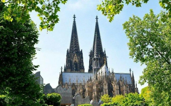 Cologne Cathedral framed by trees on a sunny day, part of a self-guided walking tour.