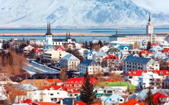 Colorful rooftops and church spires in Reykjavik, Iceland, with snowy mountains in the background.