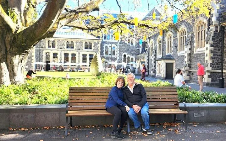 Couple sitting on a bench in front of historic stone building in Christchurch city.