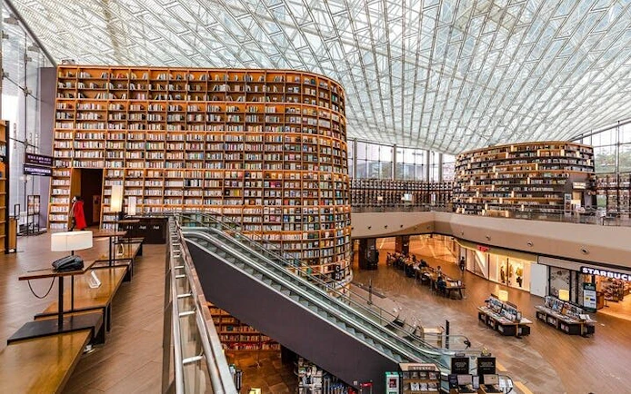 Seoul Starfield Library with towering bookshelves and escalator in modern mall setting.