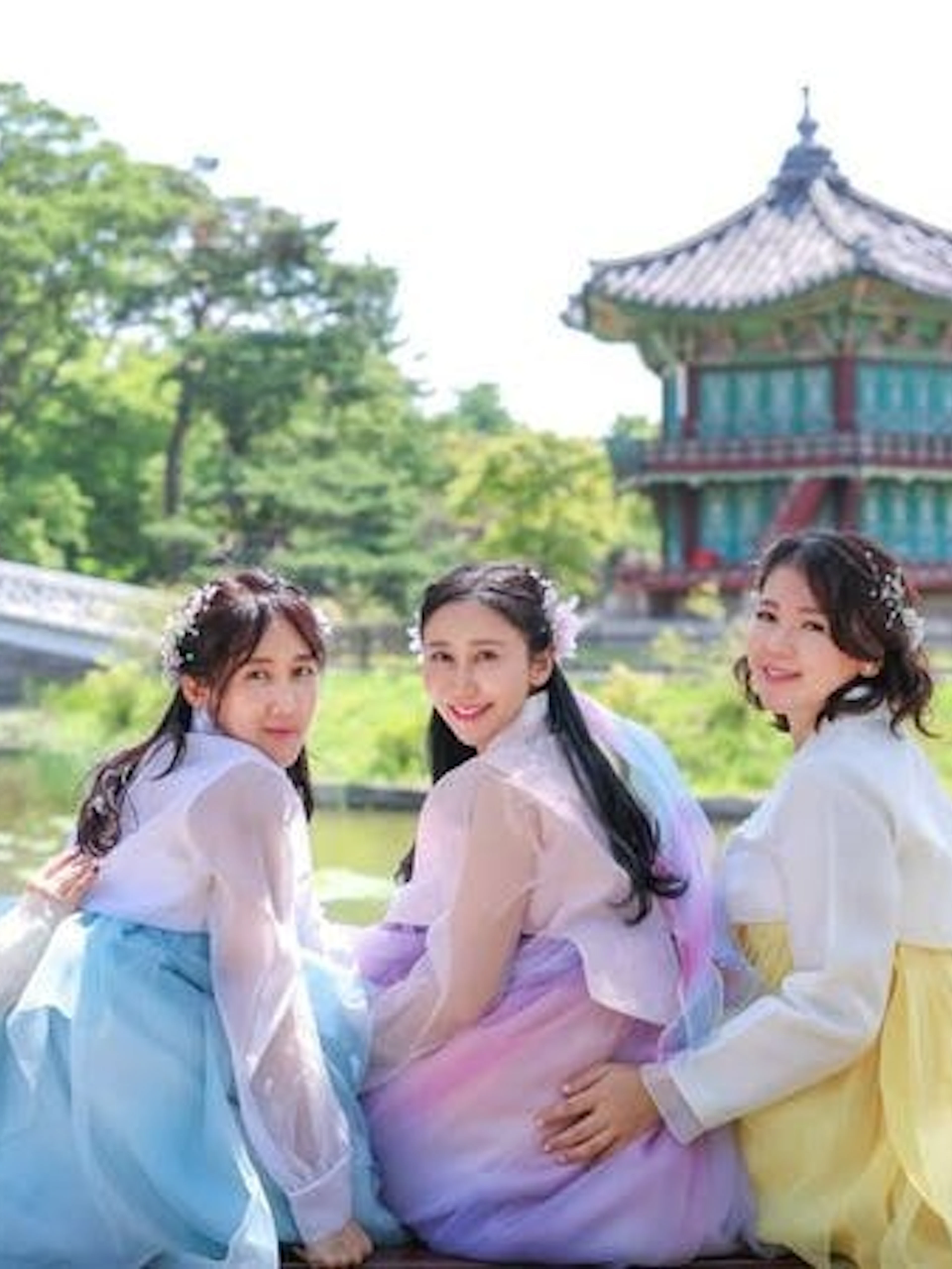 Women in hanbok at Gyeongbokgung Palace, Seoul, with traditional pavilion and pond in background.
