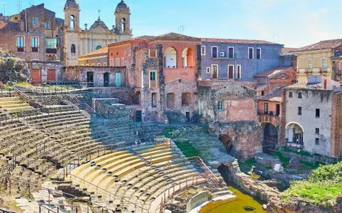 Roman amphitheater ruins in Catania, Italy, surrounded by historic buildings.
