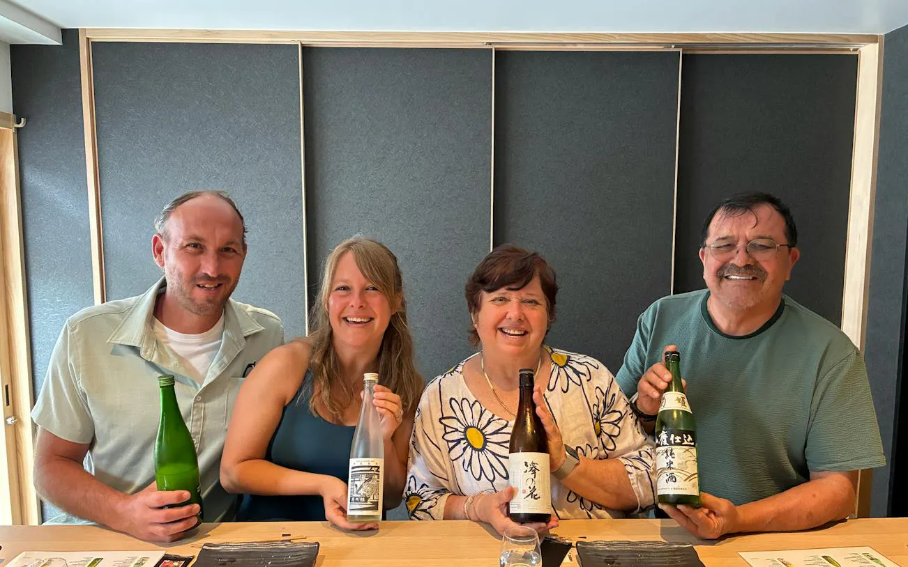Group enjoying sake tasting with a sommelier in Kyoto, holding various sake bottles.