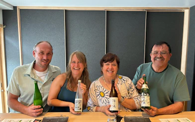 Group enjoying sake tasting with a sommelier in Kyoto, holding various sake bottles.