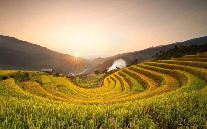 Rice terraces at sunrise in Mu Cang Chai, Vietnam, with distant ethnic village houses.