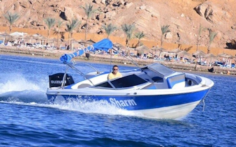 Speedboat on water near Sharm El Sheikh with rocky shoreline and palm trees in background.