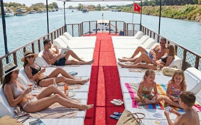 Boat tour group relaxing on deck with drinks, Antalya river view, part of Lower Duden Waterfall tour.