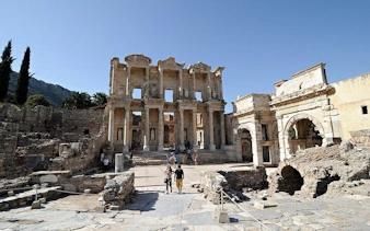 Ephesus Library ruins with tourists exploring ancient site on a sunny day.