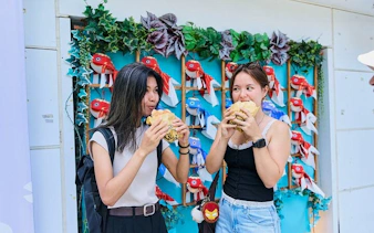 Two people enjoying street food in Asakusa, Tokyo, with colorful fish decorations in the background.