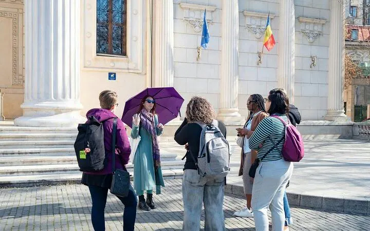Tour guide with purple umbrella leading a group in front of historic building in Bucharest Old Town.