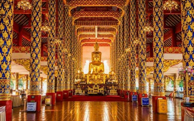 Golden Buddha statue inside Wat Suan Dok temple, Chiang Mai, with ornate columns and intricate designs.