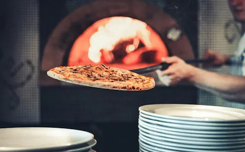 Neapolitan pizza being placed in a wood-fired oven during a cooking class in Naples.