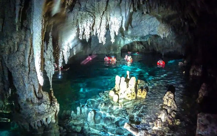 Snorkelers explore a cenote with stalactites and clear water on a guided tour in Mexico.