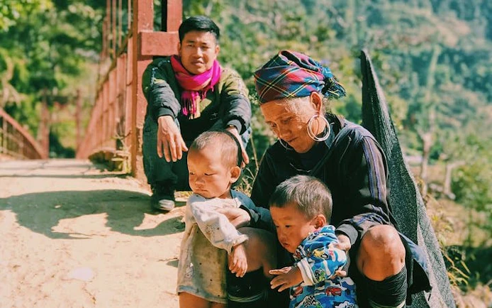 Elderly woman with children on a path in Ta Van Village, Sapa, with a man sitting nearby.