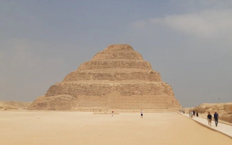 Step Pyramid of Djoser at Saqqara with tourists walking nearby.