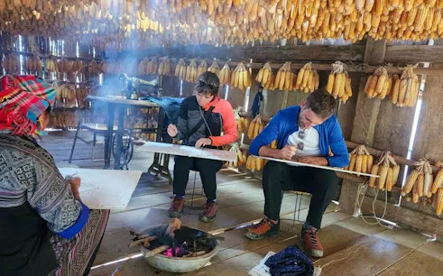 Local Hmong guide teaching traditional beeswax painting to tourists in Mu Cang Chai.