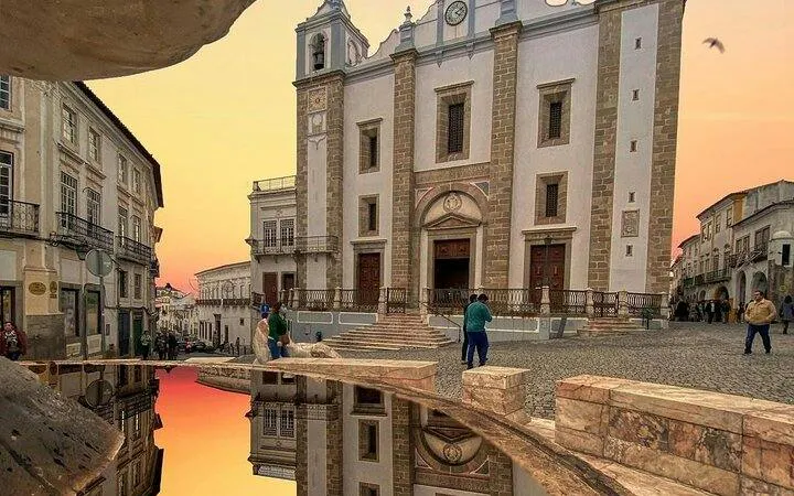 Évora town square with historic church at sunset, reflecting in a fountain, Alentejo region.