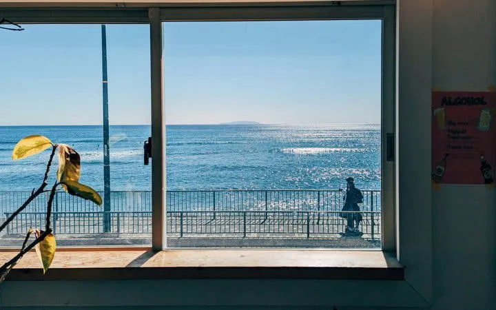 View of the ocean from a window in Kamakura, with a person walking along the seaside path.