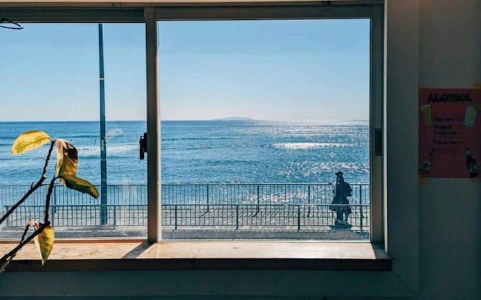 View of the ocean from a window in Kamakura, with a person walking along the seaside path.