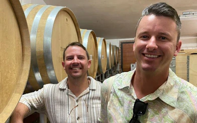 Visitors in a Tuscan winery cellar with large wooden barrels during a small-group wine tour.