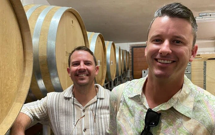 Visitors in a Tuscan winery cellar with large wooden barrels during a small-group wine tour.