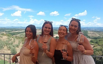 Women enjoying wine tasting with a view of Tuscan vineyards on a Pisa and Vinci day tour.