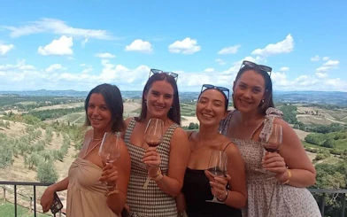 Women enjoying wine tasting with a view of Tuscan vineyards on a Pisa and Vinci day tour.