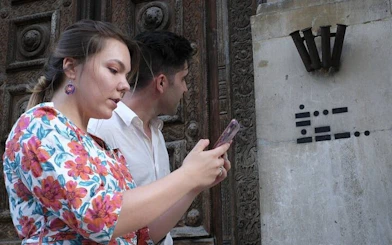 Exploring Budapest with a self-guided city game, couple using phone near historic building.