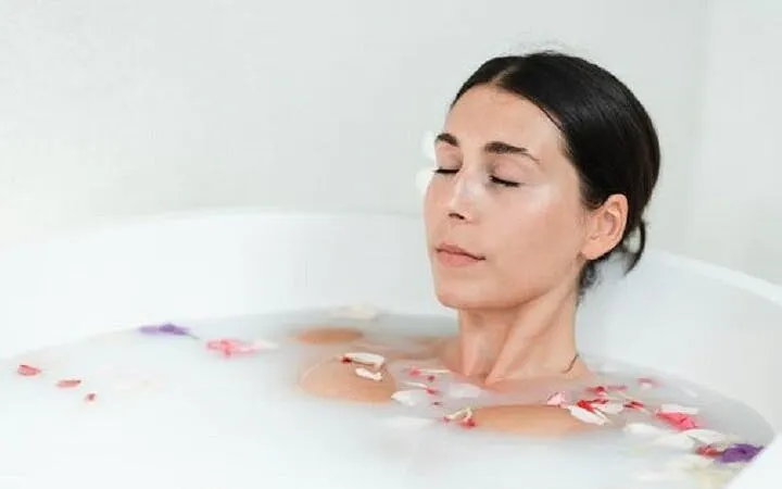 Woman relaxing in a milk bath with flower petals during a Moroccan Hammam experience in Marrakesh.