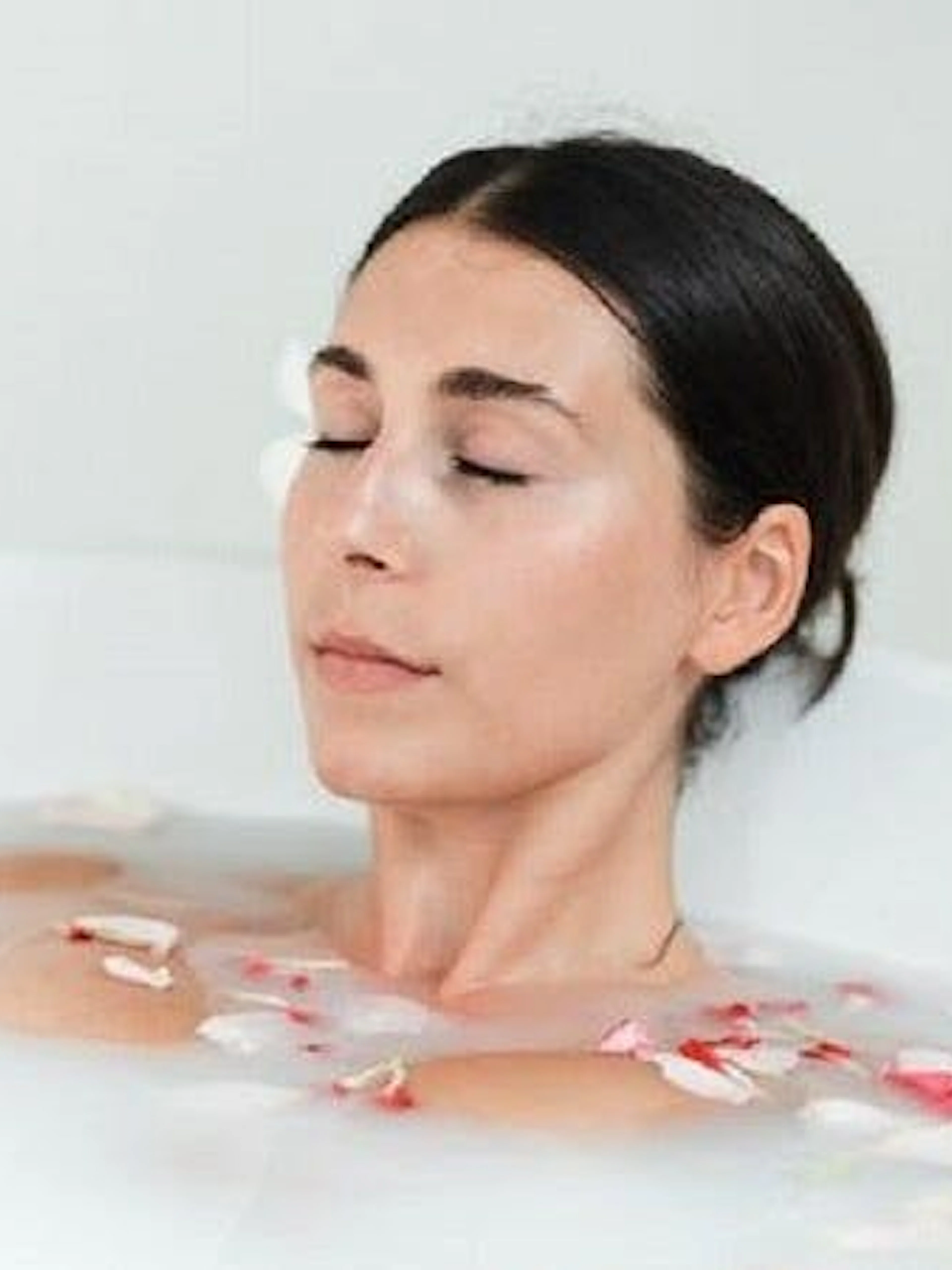 Woman relaxing in a milk bath with flower petals during a Moroccan Hammam experience in Marrakesh.