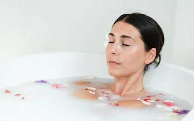 Woman relaxing in a milk bath with flower petals during a Moroccan Hammam experience in Marrakesh.
