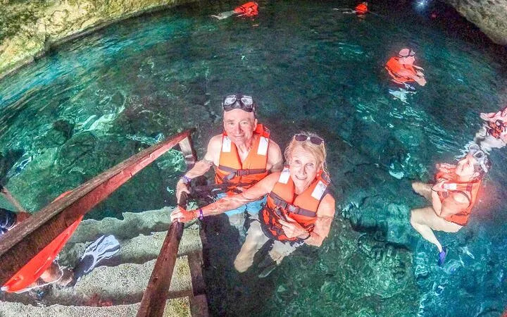 Visitors swimming in a cenote cave with life jackets during a guided tour in Akumal, Mexico.