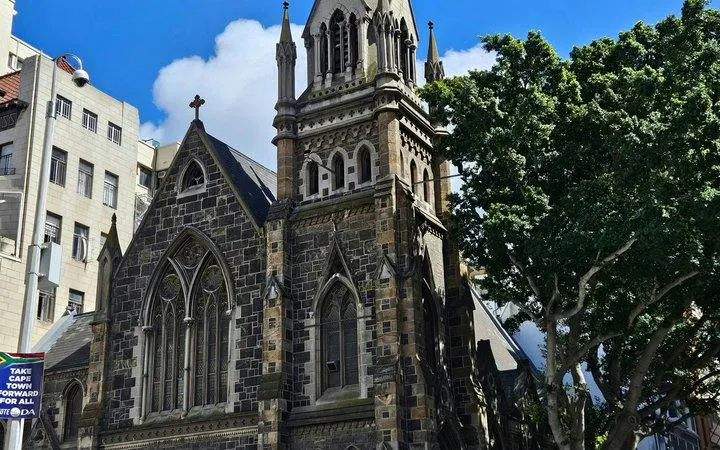 Historic stone church in Cape Town with gothic architecture, surrounded by city buildings and trees.
