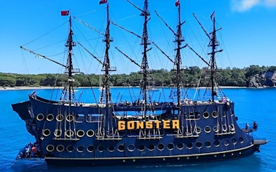 Pirate ship GONSTER on blue waters near Kemer, Turkey, with lush coastline in background.