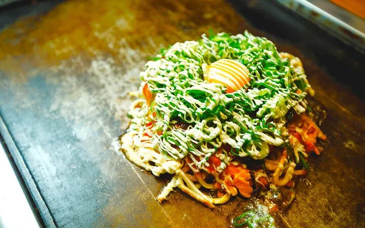 Okonomiyaki cooking on a griddle during Osaka street food tour in Dotonbori and Namba.