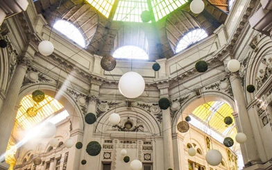 Ceiling of historic arcade in Old Town Bucharest with hanging spheres and sunlight streaming through.