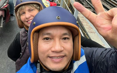 Two people wearing helmets on a Vespa during a Hanoi street tour.